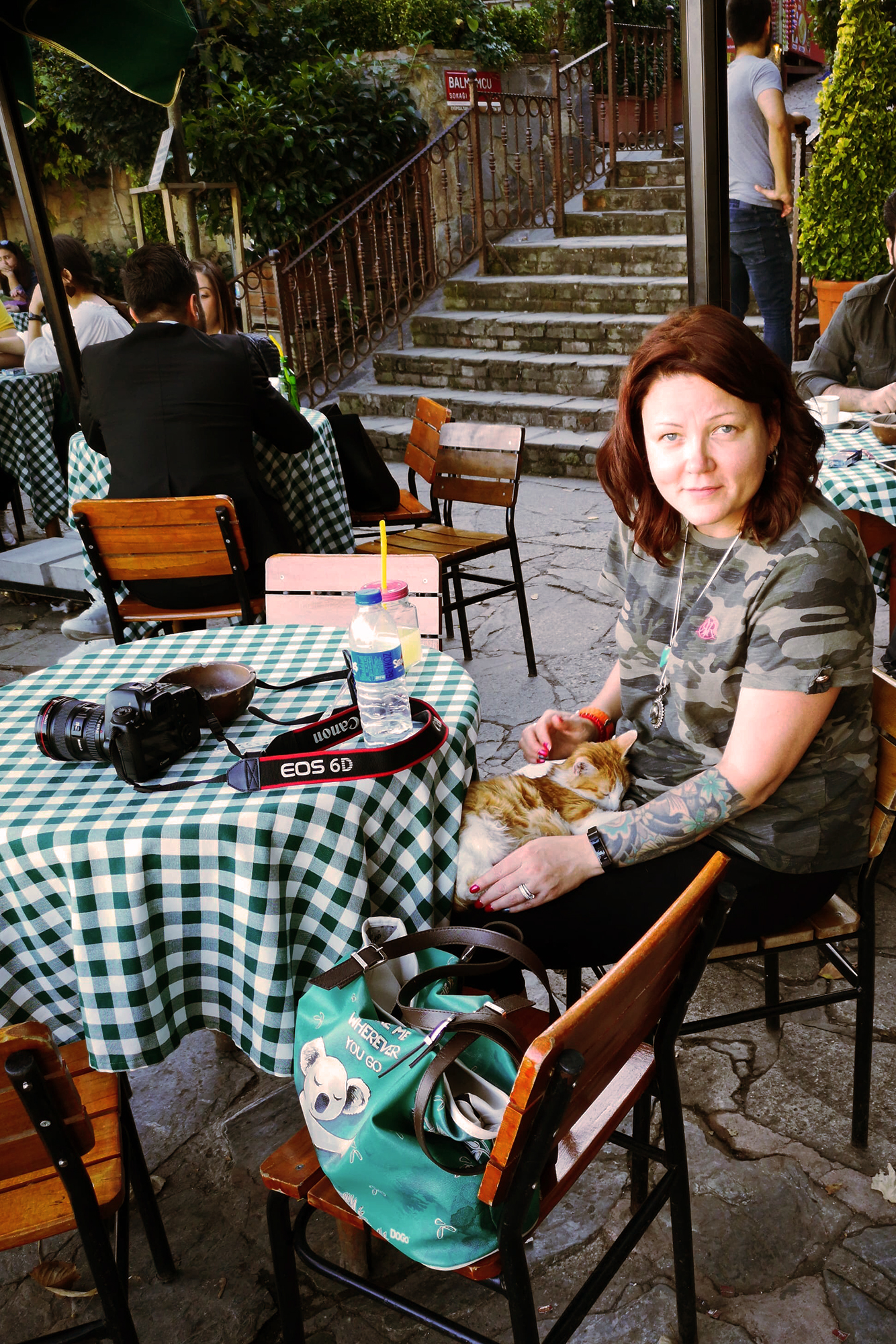 charnette kvinna sitter på ett kafé med en katt i knät